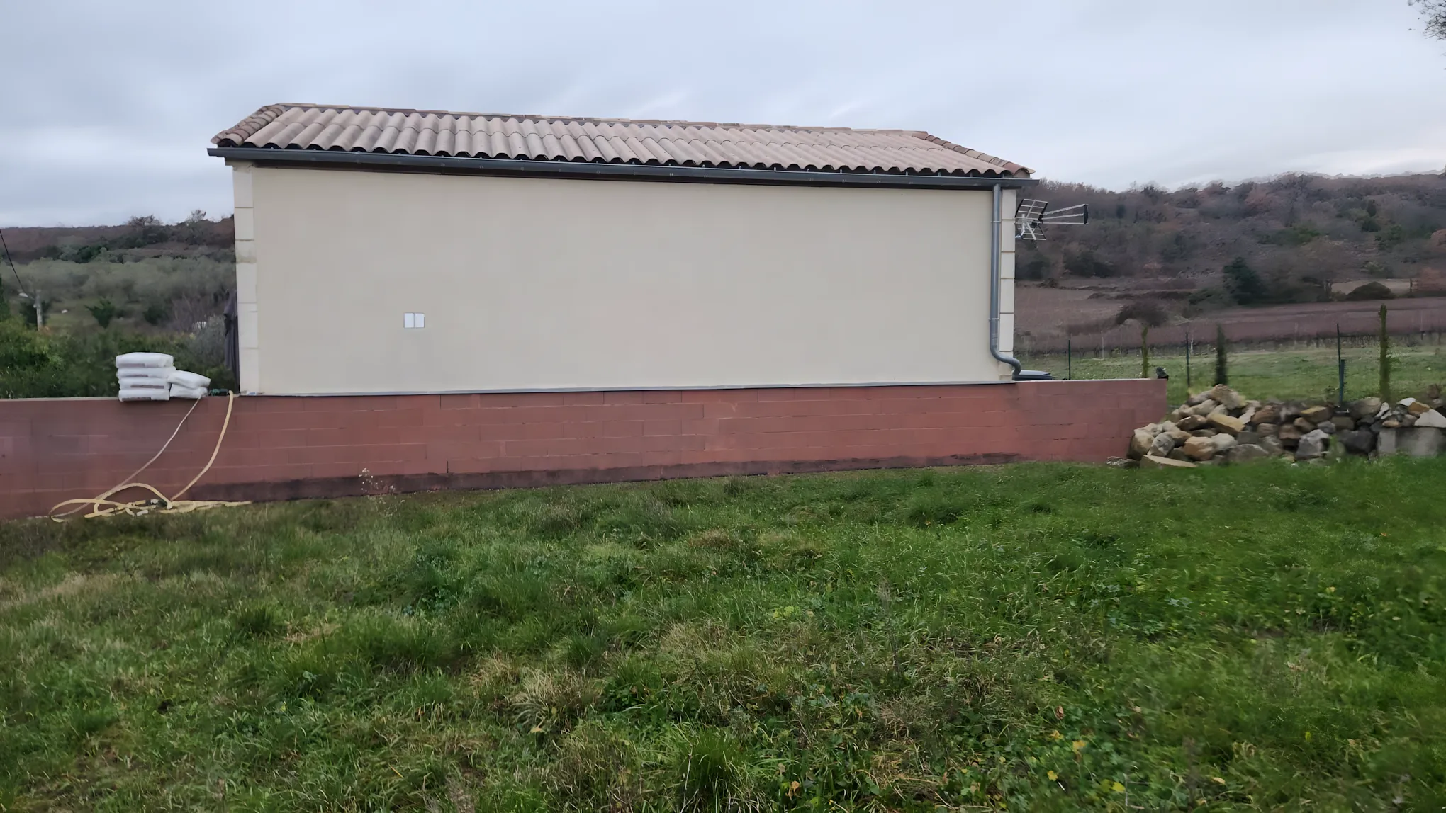 Muret en parpaings bruts avant travaux, façade enduite en arrière-plan